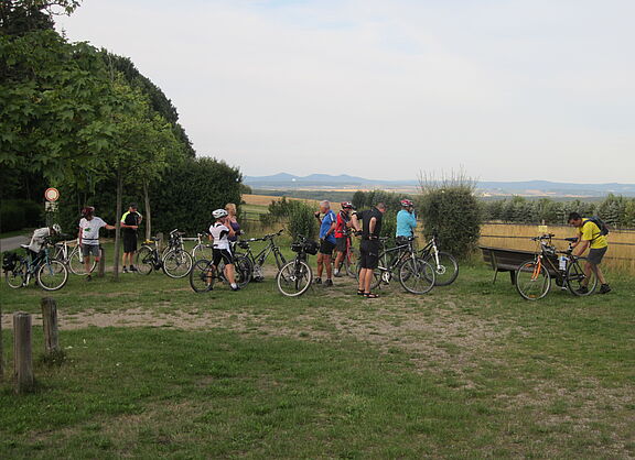 Das Bild zeigt eine Radlergruppe während einer Rast, im Hintergrund ein weiter Blick auf das Siebengebirge
