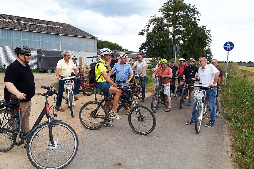 Tour Kommunalpolitik August 2022 Das Foto zeigt eine Grppe von Kommunalpolitiker_Innen und de ADFC bei einem Halt auf dem neuen Radweg hinter dem Gut Holzem in Berkum. Zu sehen sind ADFC-Verkehrsexperte Jörg Landmann, der Bürgermeister Jörg Schmidt und den Teilnehmenden die Einschätzung des ADFC zu diesem Projekt erläutert.